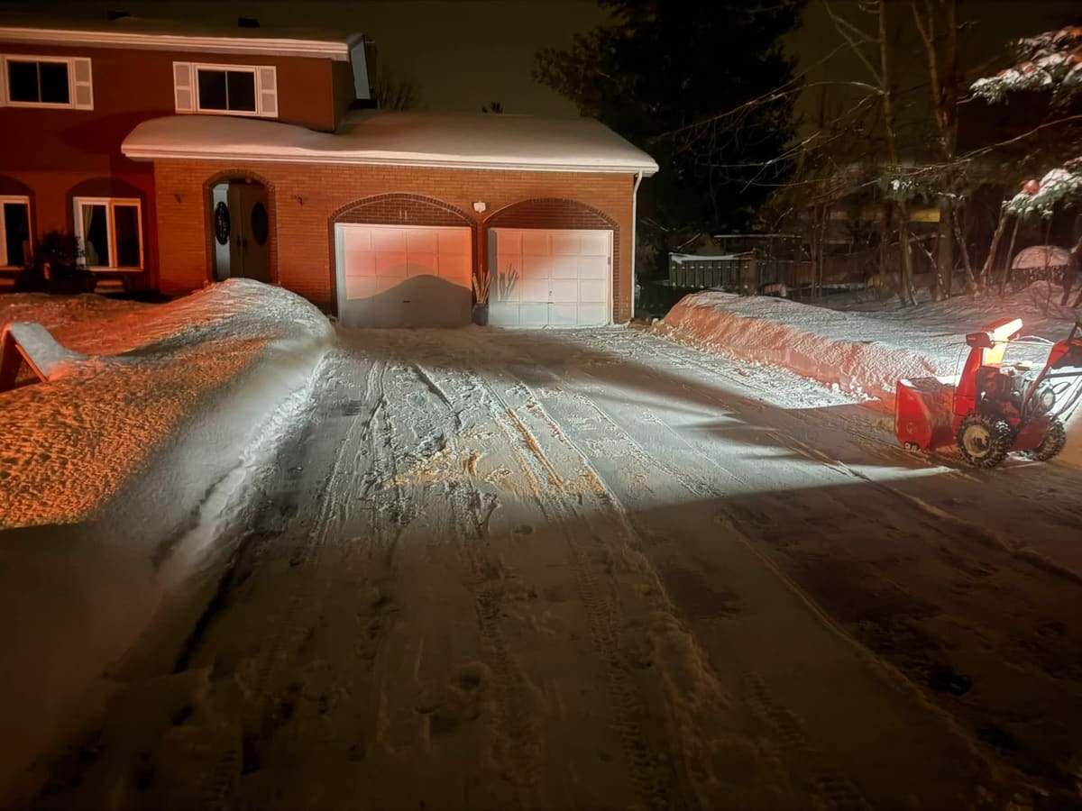 Snowblower with headlight running at night on a freshly cleared driveway